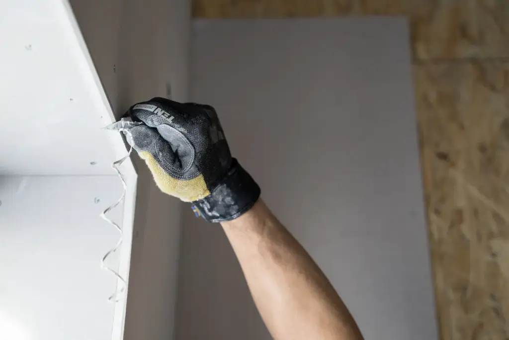 Close-up of a gloved hand applying plaster to a wall indoors